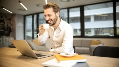 depth of field photo of man sitting on chair while holding cup in front of table